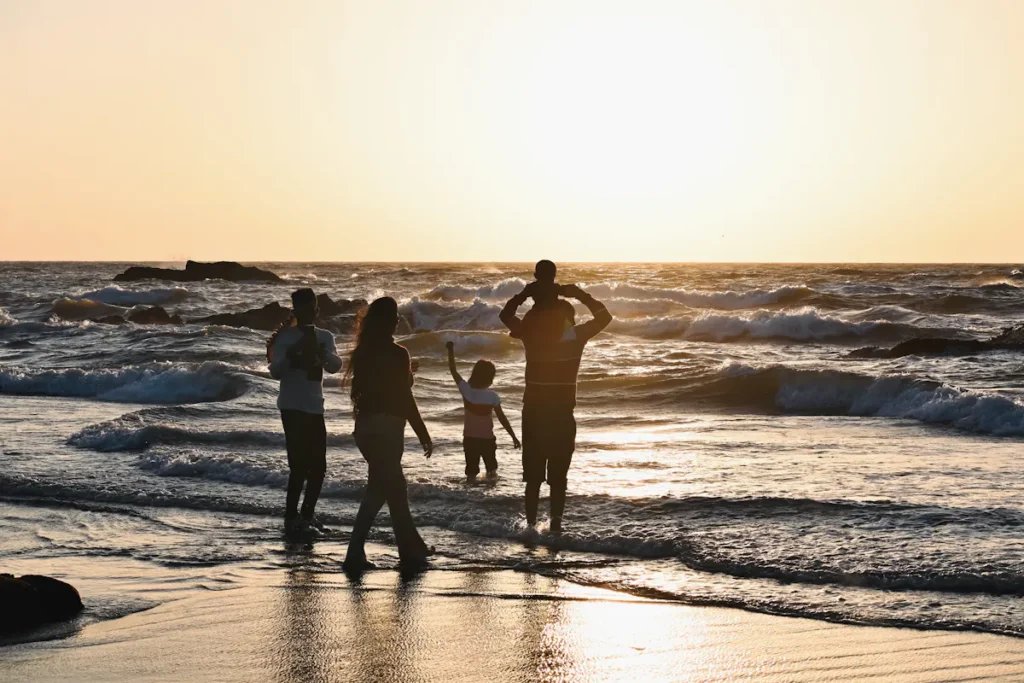 Família a caminhar junta numa praia ao pôr do sol, vista de costas